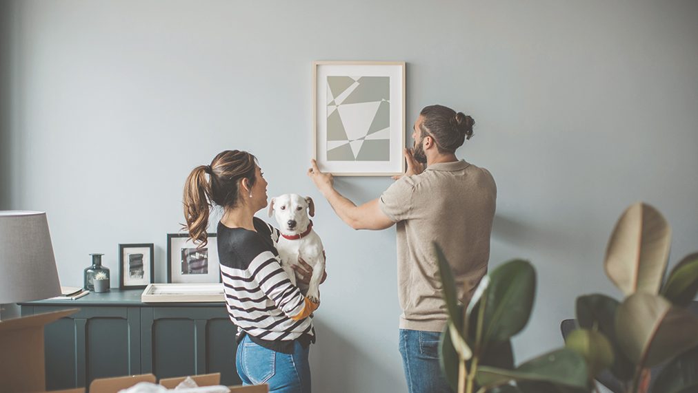Couple with dog adjusting a painting on the wall